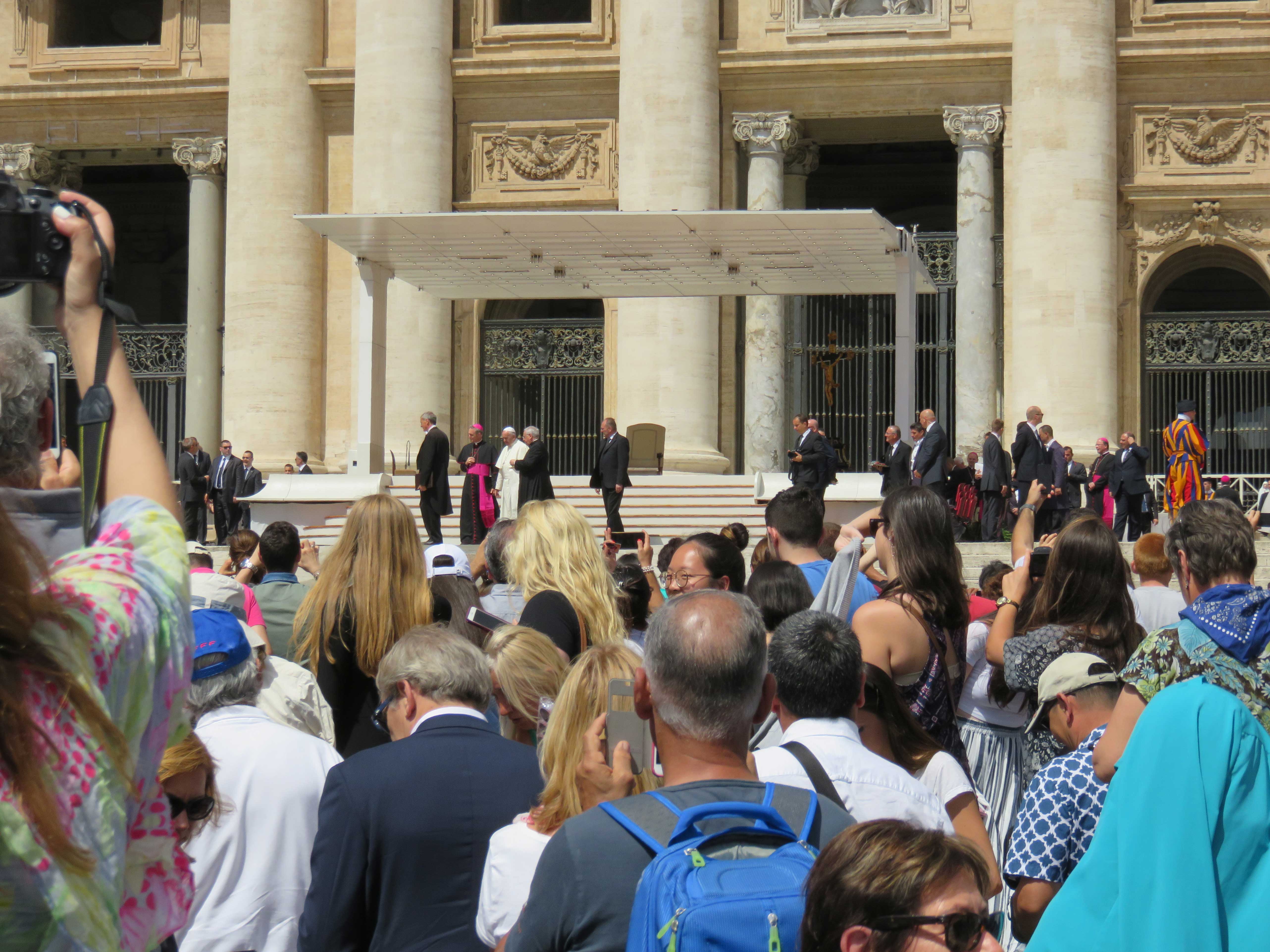 Vorne viele Gläubige, hinten Papst Franzikus