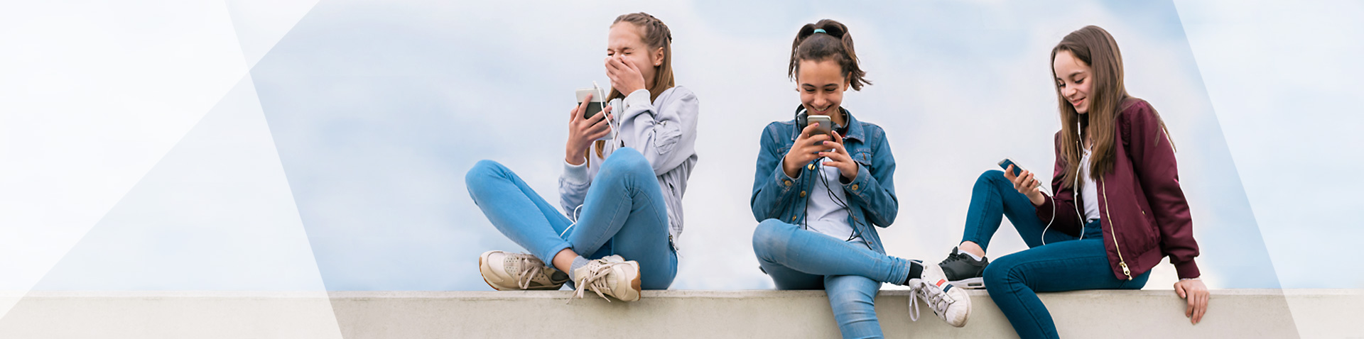 Drei junge Mädchen sitzen auf einer Mauer und halten Handys in den Händen.