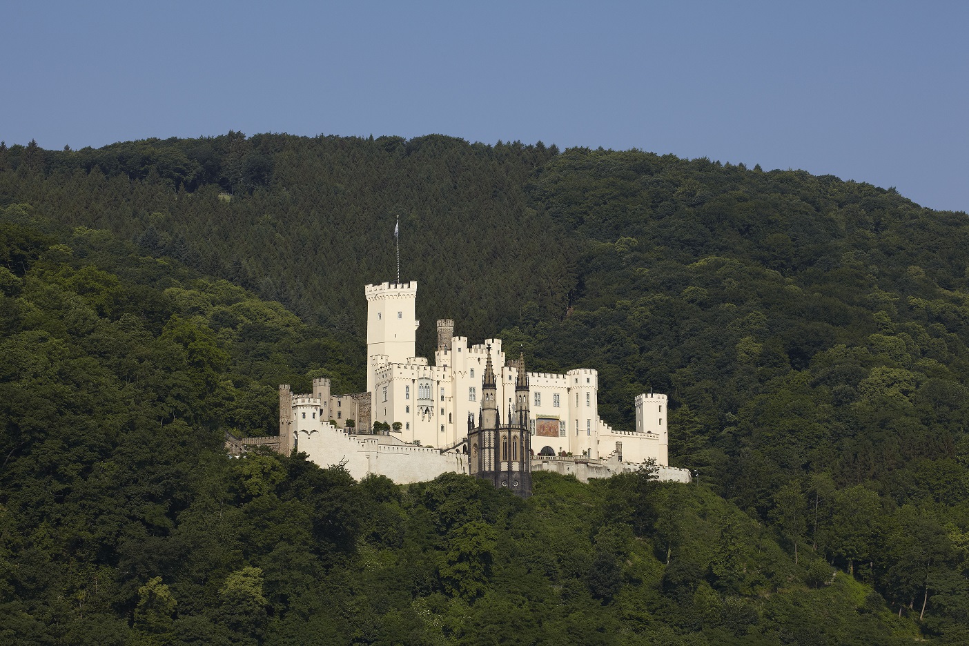 Helles Schloss, an einem Berghang, umgeben von Bäumen 