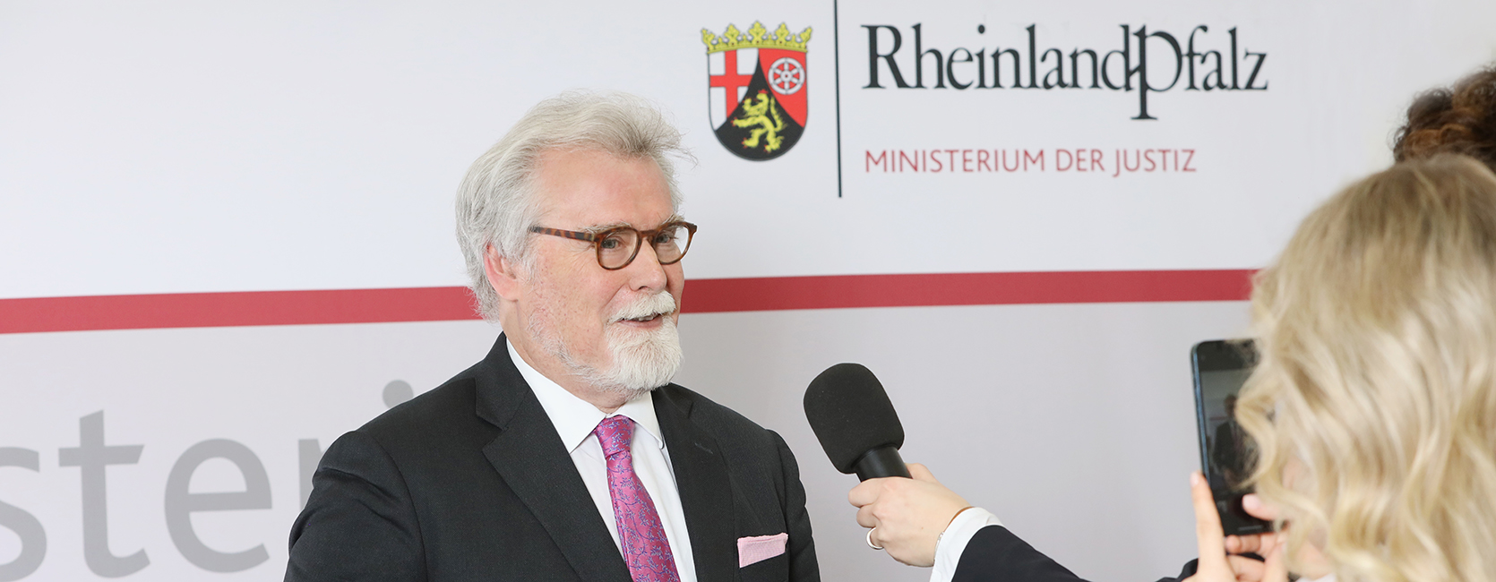 Justizminister Herbert Mertin während eines Interviews vor einer Pressewand des Ministeriums der Justiz