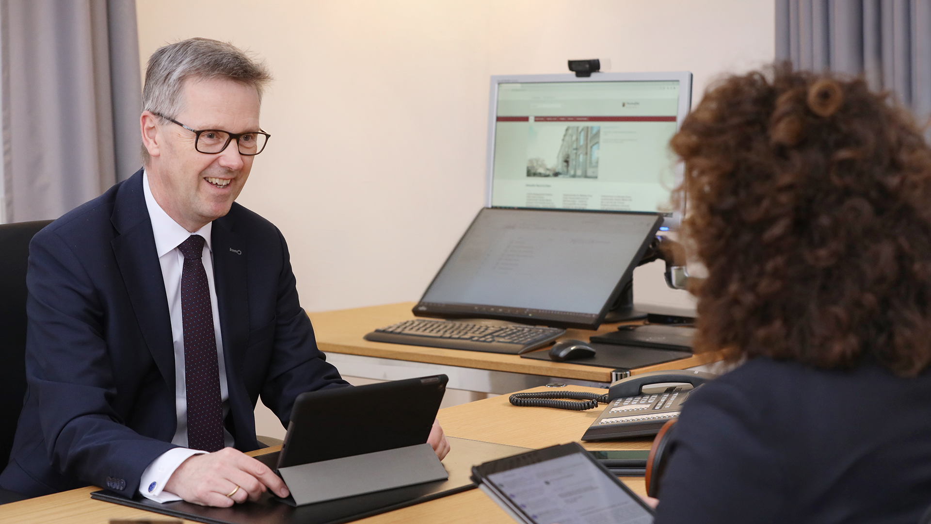 Staatssekretär Dr. Matthias Frey am Schreibtisch im Gespräch mit einer Frau mit lockigen Haaren