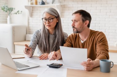 Mature middle-aged couple family wife and husband counting funds, savings declarations, investments,paperwork, financial documents, bankruptcy, court case, bills, pension with laptop.