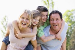 Famielienbild: Mutter trägt ein Kind Huckepack, zweites Kind und Vater