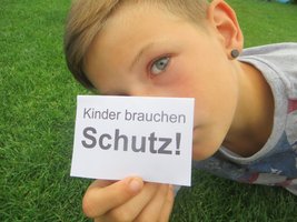 Kind hält Schild mit der Aufschrift "Kinder brauchen Schutz" in der Hand